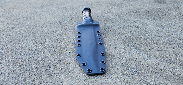 A custom Kydex sheath for a 7" fullsize KA-BAR USMC fighting knife, displayed on a textured surface.