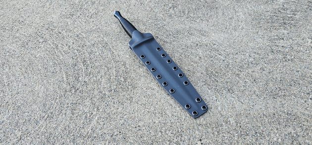 A custom Kydex sheath for a Fairbairn Sykes Commando Dagger knife, displayed on a textured surface.