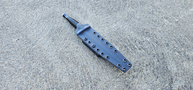 A custom Kydex sheath for a Fairbairn Sykes Commando Dagger knife, displayed on a textured surface.