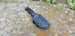 A black pancake style custom kydex sheath with polymer belt clip for a knife, placed on a textured surface.